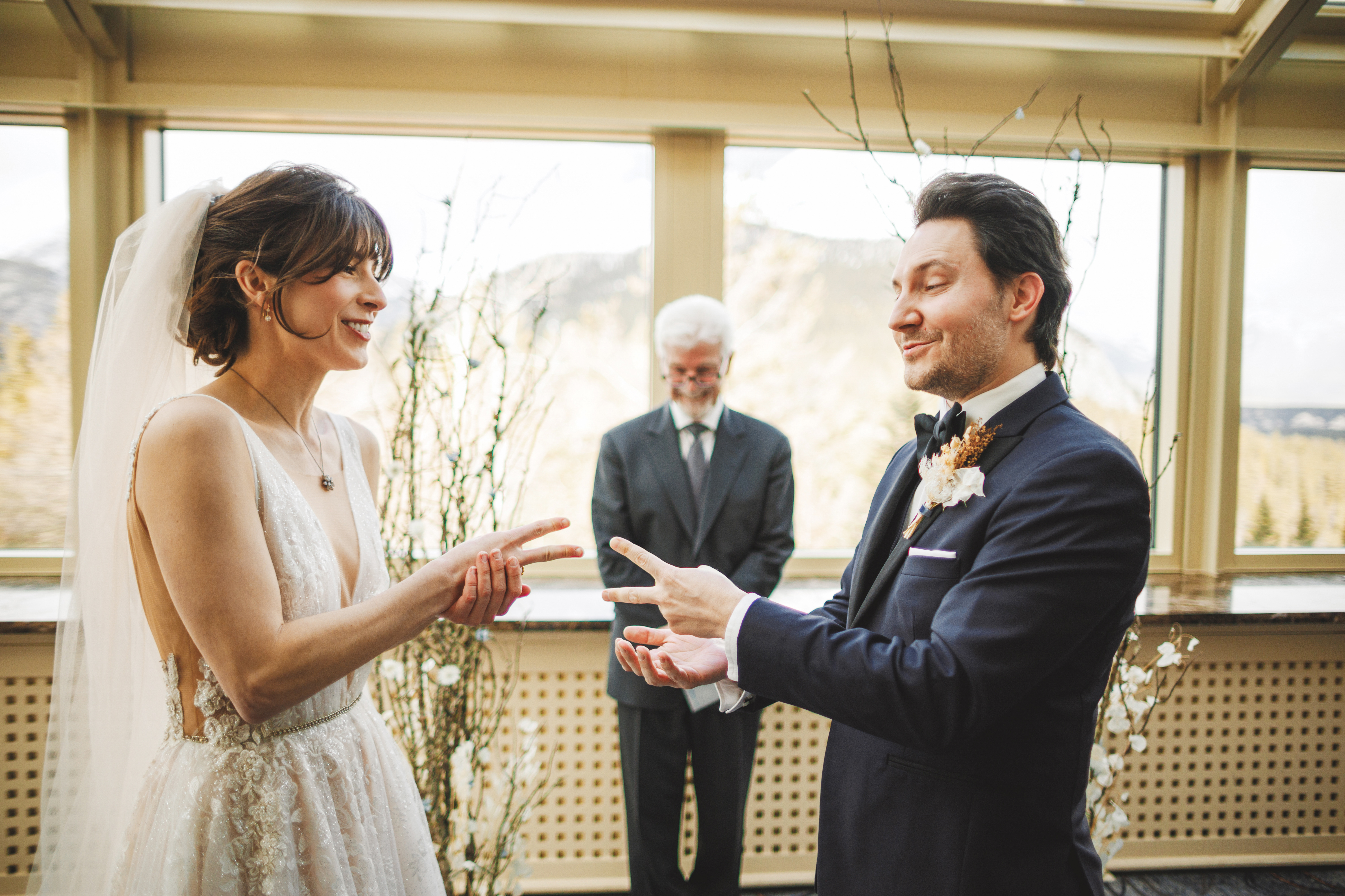 A bride and groom play rock-paper-scissors during their wedding ceremony as an officiant stands behind them.