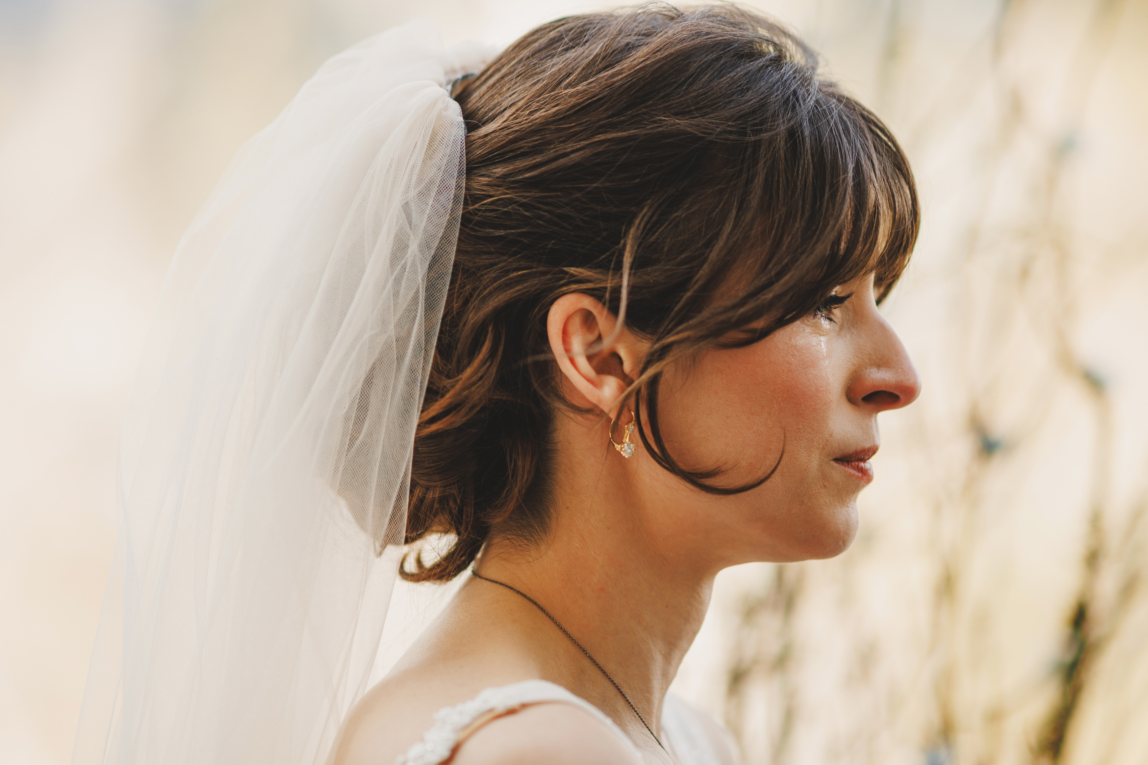 A woman in a white wedding dress and veil is shown in profile, looking ahead with a serious expression and a tear on her cheek.