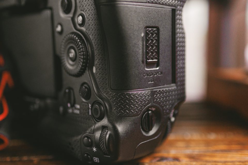 Close-up of the side of a black digital camera showing textured grip, buttons, and memory card compartment labeled "CARD OPEN. Close-up of the side of a black digital camera showing textured grip, buttons, and memory card compartment labeled "CARD OPEN.