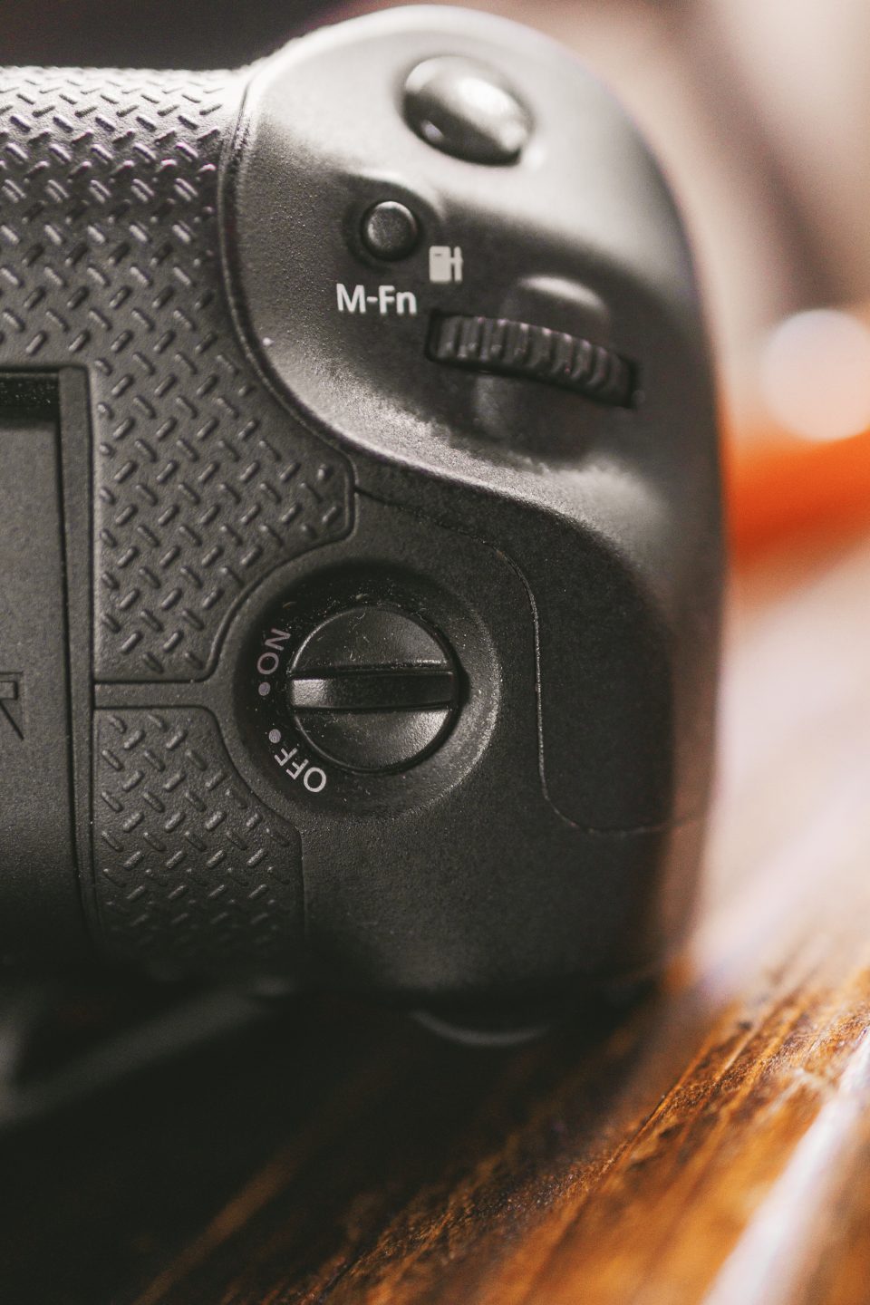 Close-up of a black camera grip showing a textured surface, a dial with "OFF" and "ON" settings, and an "M-Fn" button next to a control wheel. Close-up of a black camera grip showing a textured surface, a dial with "OFF" and "ON" settings, and an "M-Fn" button next to a control wheel.