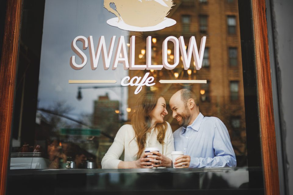 A man and woman sit together indoors, smiling and holding coffee cups at a window counter in Swallow Cafe. A man and woman sit together indoors, smiling and holding coffee cups at a window counter in Swallow Cafe.