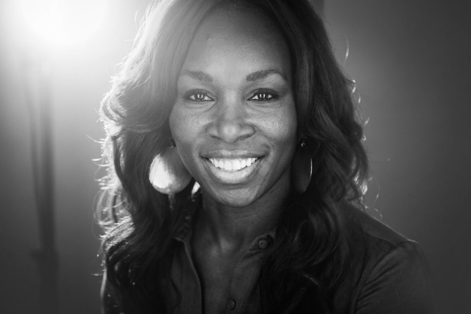 A woman with long wavy hair smiles at the camera, wearing a collared shirt and large circular earrings, in a softly lit setting—captured by a talented DC portrait photographer. A woman with long wavy hair smiles at the camera, wearing a collared shirt and large circular earrings, in a softly lit setting—captured by a talented DC portrait photographer.
