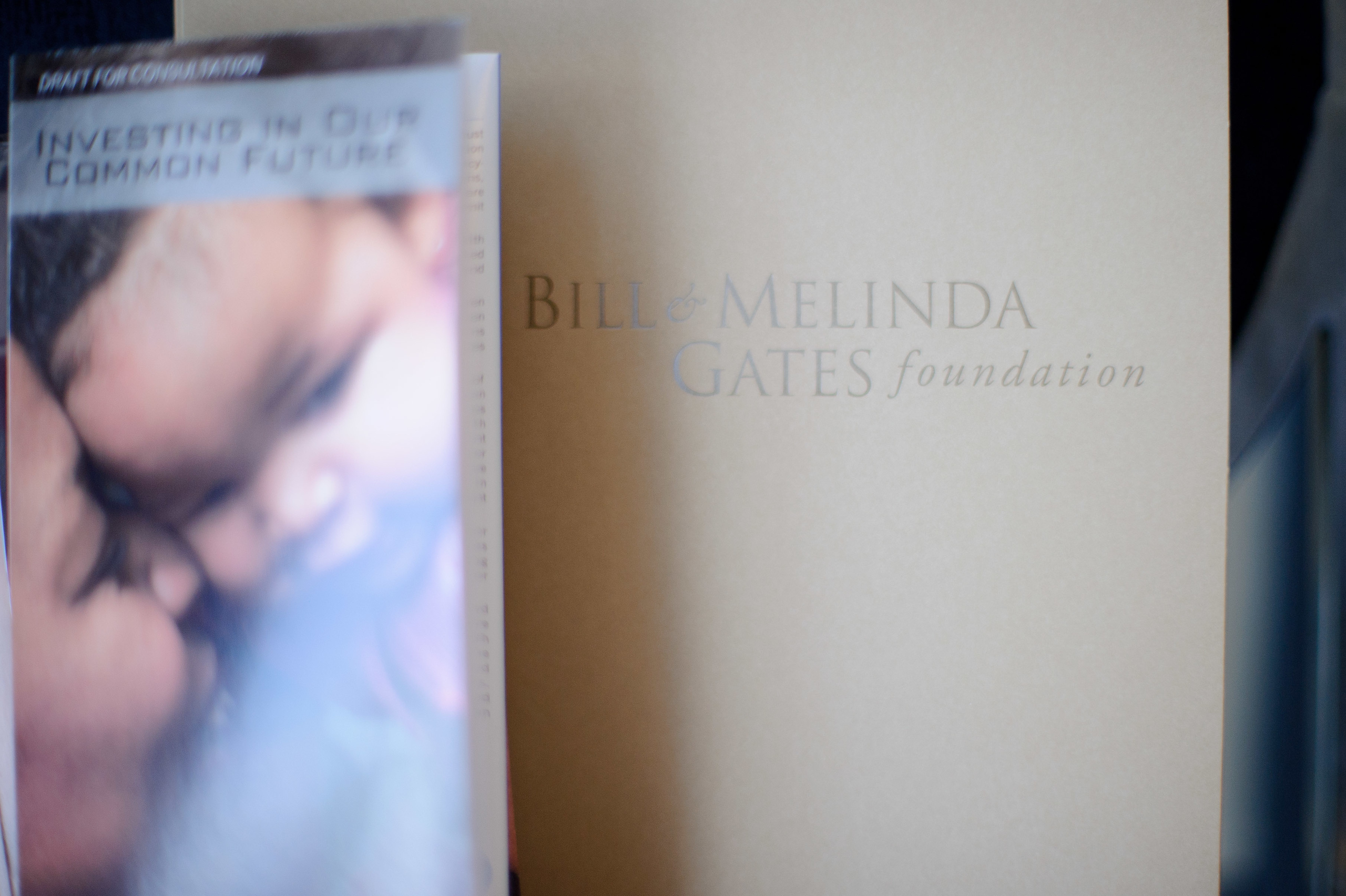 A brochure titled "Investing in Our Common Future" rests next to a folder labeled "Bill & Melinda Gates Foundation.