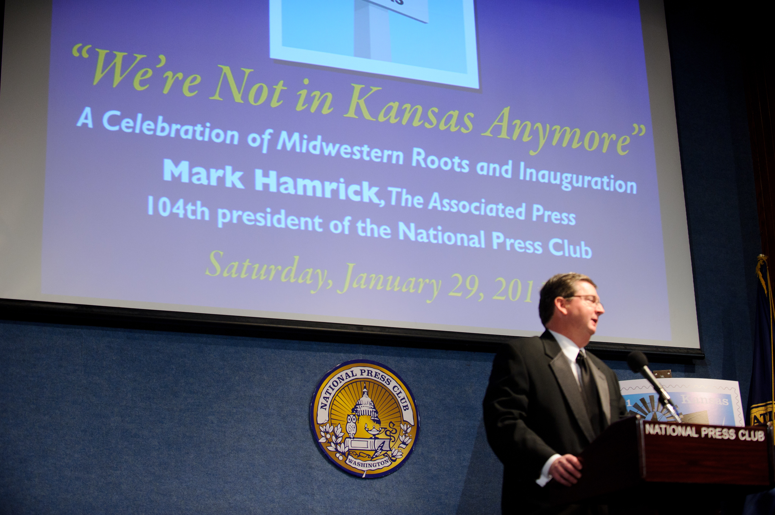 A man speaks at a podium in front of a presentation slide titled "We're Not in Kansas Anymore" at the National Press Club event on January 29, 2011.